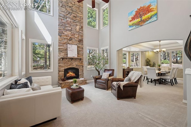 carpeted living room with baseboards, arched walkways, a high ceiling, an inviting chandelier, and a stone fireplace