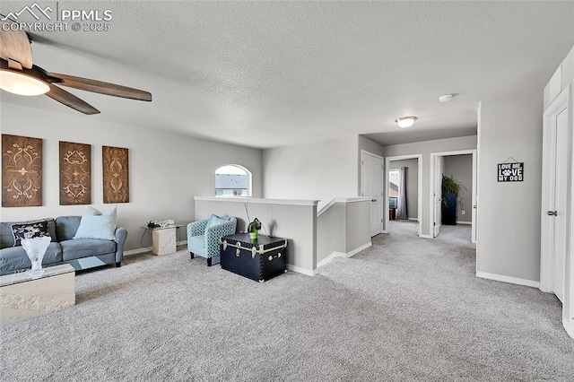 living room featuring light carpet, a ceiling fan, a textured ceiling, and baseboards