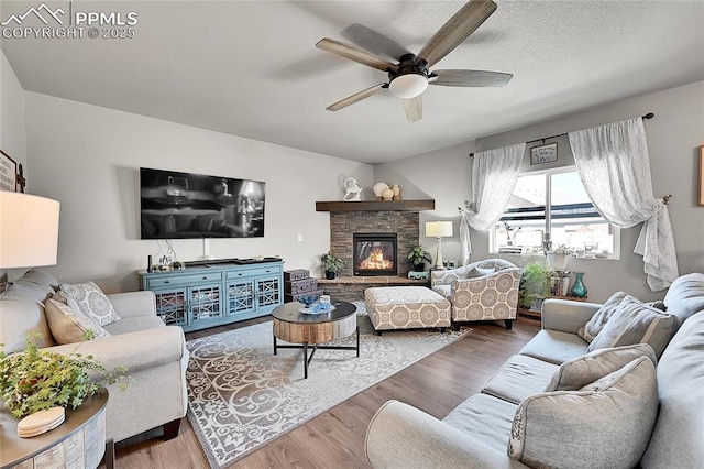 living area with a stone fireplace, wood finished floors, and ceiling fan