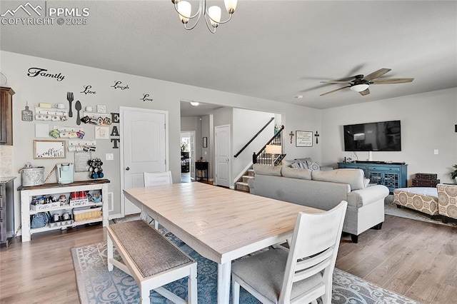 dining area featuring ceiling fan with notable chandelier, wood finished floors, and stairway