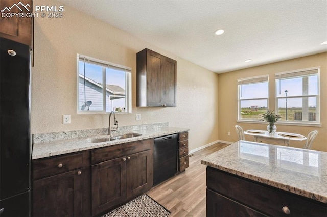 kitchen featuring light wood finished floors, light stone counters, a sink, dark brown cabinetry, and black appliances