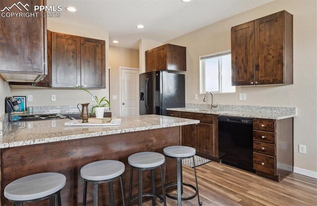 kitchen featuring a sink, black appliances, a breakfast bar area, light wood finished floors, and a peninsula