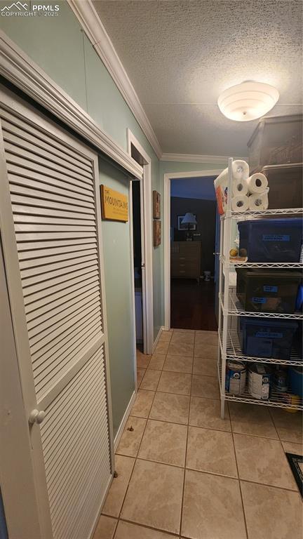 hallway featuring ornamental molding, a textured ceiling, and light tile patterned floors