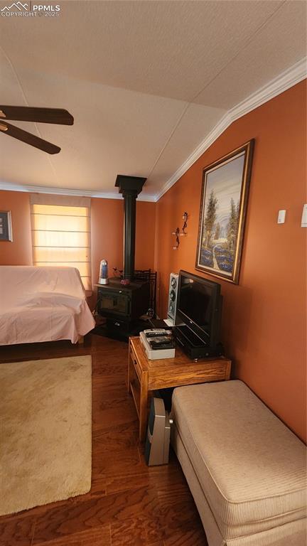 bedroom with wood finished floors, crown molding, lofted ceiling, a wood stove, and ceiling fan