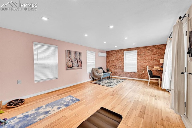 living area featuring an AC wall unit, light wood-type flooring, baseboards, recessed lighting, and brick wall