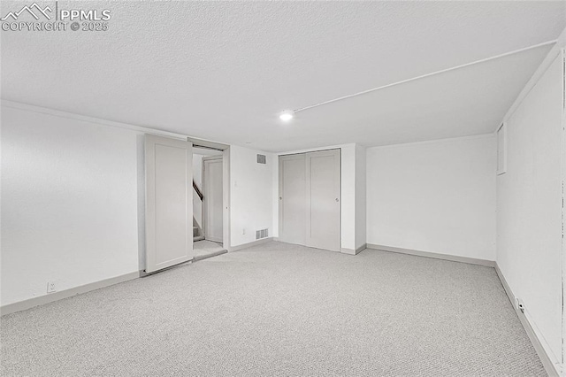 interior space with a textured ceiling, baseboards, visible vents, and light colored carpet