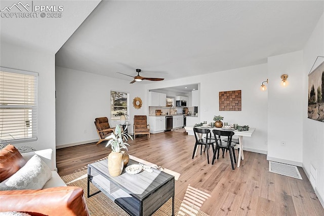 living area featuring baseboards, a ceiling fan, and light wood finished floors