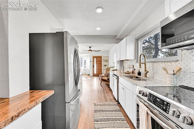 kitchen featuring a sink, light wood-style floors, tasteful backsplash, appliances with stainless steel finishes, and white cabinetry