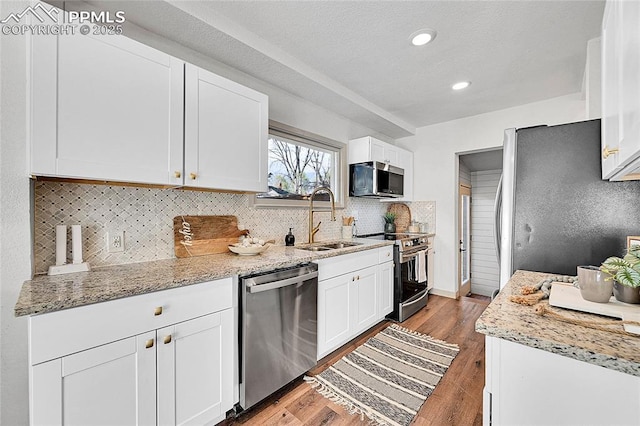 kitchen with stainless steel appliances, a sink, backsplash, and white cabinetry