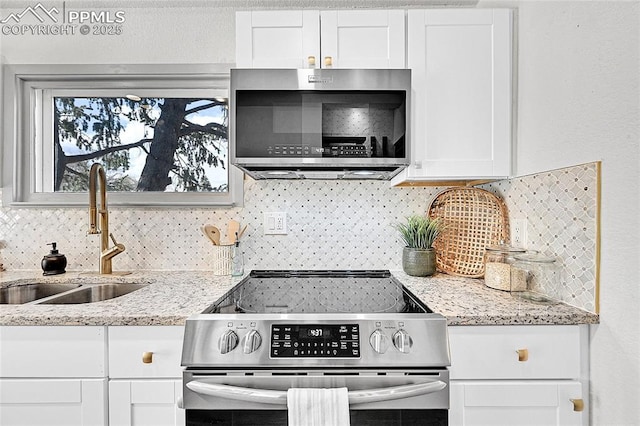 kitchen featuring white cabinets, stainless steel appliances, a sink, decorative backsplash, and light stone countertops