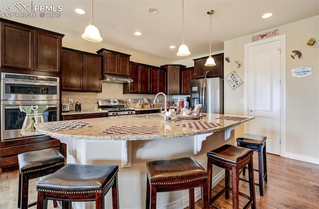 9825 Golf Crest Dr, Peyton, CO 80831 - kitchen with a sink, light wood-type flooring, under cabinet range hood, stainless steel appliances, and a breakfast bar area