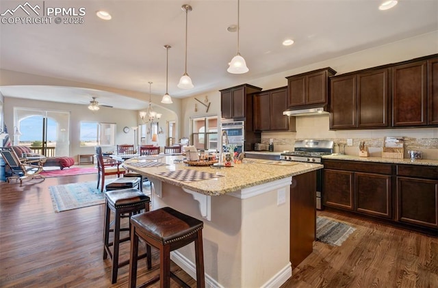 9825 Golf Crest Dr, Peyton, CO 80831 - kitchen with under cabinet range hood, stainless steel gas range, dark wood-style flooring, and dark brown cabinets