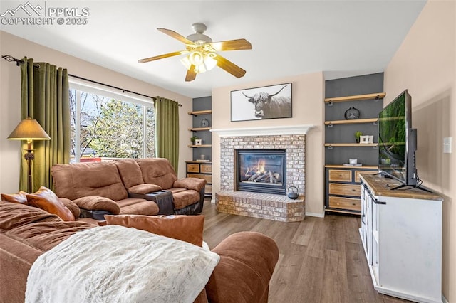 living area with a brick fireplace, a ceiling fan, and wood finished floors