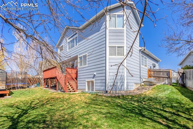 back of house featuring a deck, a yard, a trampoline, a fenced backyard, and stairs