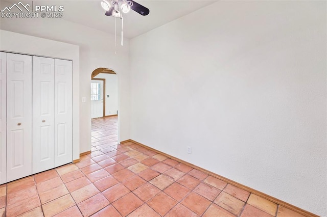 unfurnished bedroom with light tile patterned floors, arched walkways, a closet, a ceiling fan, and baseboards