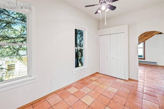 unfurnished bedroom featuring baseboard heating, arched walkways, and multiple windows