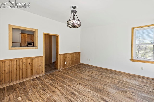 empty room featuring wooden walls, a wainscoted wall, and wood finished floors