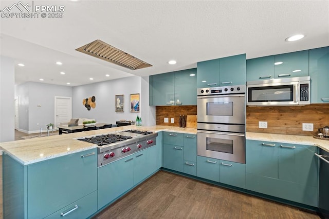kitchen with a peninsula, light stone countertops, dark wood-type flooring, decorative backsplash, and stainless steel appliances