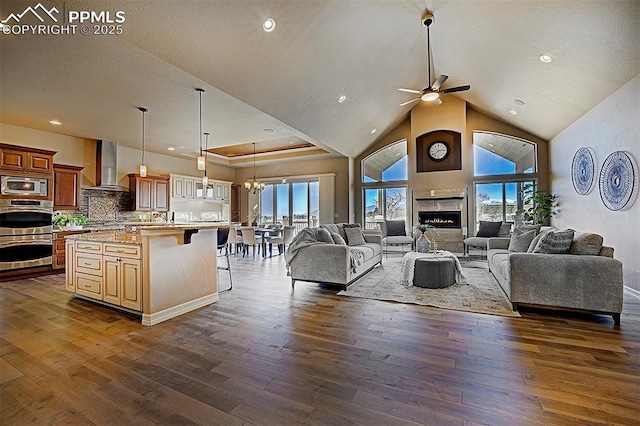 living area with dark wood-style flooring, a large fireplace, recessed lighting, high vaulted ceiling, and ceiling fan with notable chandelier