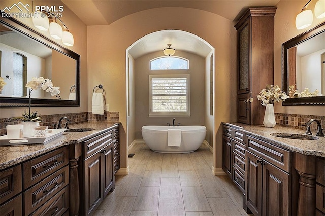 bathroom with tasteful backsplash, baseboards, a sink, and a freestanding tub