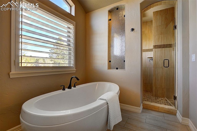 full bath with baseboards, wood finished floors, a stall shower, and a soaking tub