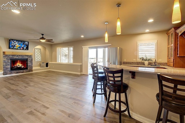 kitchen featuring decorative light fixtures, ceiling fan, freestanding refrigerator, a kitchen breakfast bar, and light stone counters