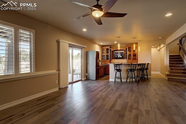 interior space with glass insert cabinets, a ceiling fan, a peninsula, a kitchen bar, and dark wood-style floors