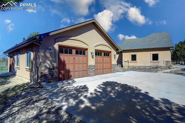 view of property exterior with stone siding, a garage, stucco siding, an outbuilding, and driveway