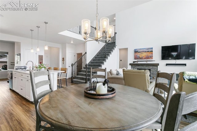 dining space featuring dark wood-type flooring, stairs, a chandelier, a stone fireplace, and a high ceiling