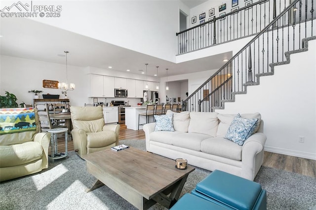 living room featuring wood finished floors, a chandelier, a towering ceiling, stairs, and baseboards