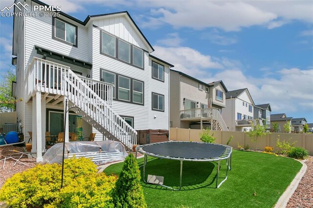 back of property with a trampoline, stairway, a residential view, a wooden deck, and board and batten siding