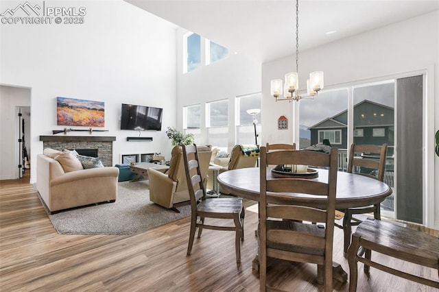 dining room featuring a fireplace, wood finished floors, a chandelier, and a high ceiling