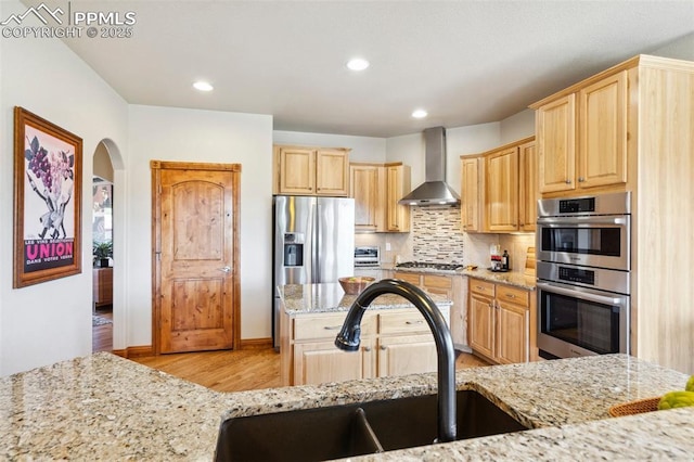 kitchen with stainless steel appliances, light wood-style flooring, a sink, wall chimney range hood, and light brown cabinets