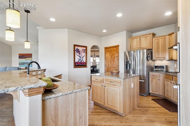kitchen with stainless steel fridge with ice dispenser, light brown cabinetry, a large island with sink, and light wood-style flooring