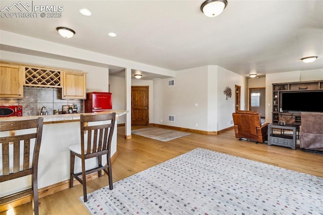 living area with wet bar, light wood-style floors, visible vents, and baseboards