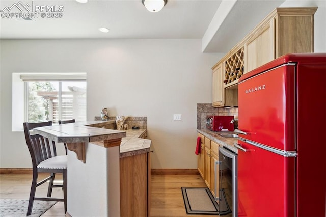 kitchen featuring light wood finished floors, a peninsula, wine cooler, freestanding refrigerator, and baseboards