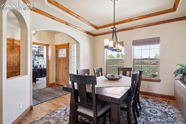 dining area featuring crown molding, a chandelier, light wood-type flooring, arched walkways, and a raised ceiling