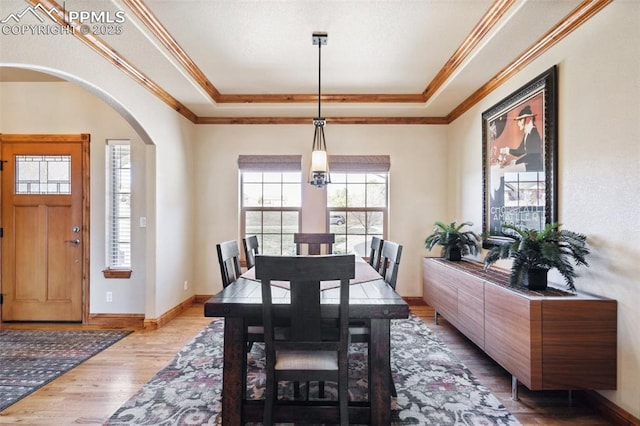 dining area featuring arched walkways, crown molding, wood finished floors, and a raised ceiling