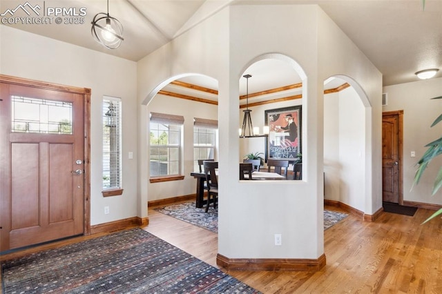 foyer with arched walkways, light wood-type flooring, vaulted ceiling, baseboards, and an inviting chandelier