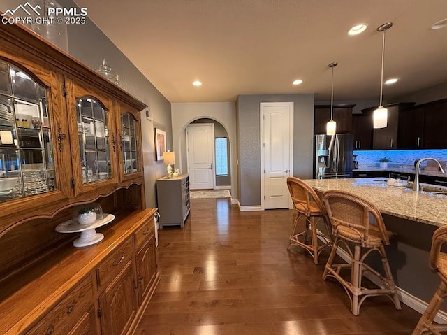 10088 Stonemont Dr, Peyton, CO 80831 - kitchen with light stone counters, a breakfast bar area, arched walkways, stainless steel refrigerator with ice dispenser, and dark wood-type flooring