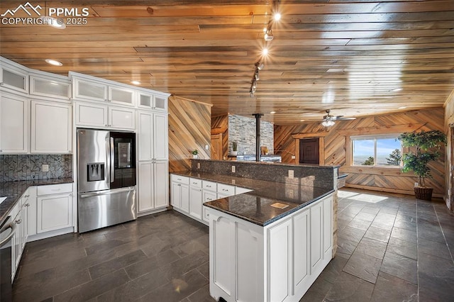 kitchen with stainless steel refrigerator with ice dispenser, a peninsula, wooden walls, and white cabinetry