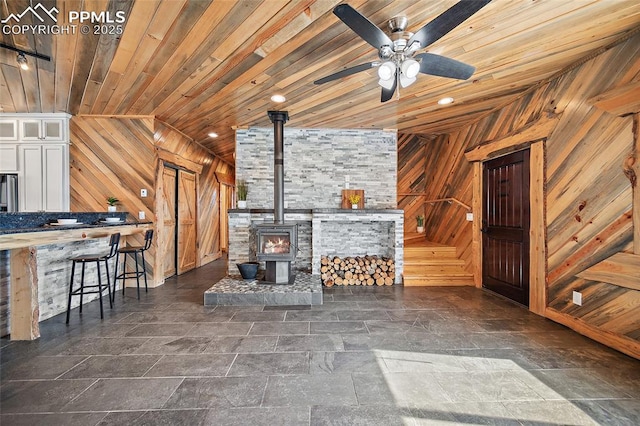 living area with wooden walls, wooden ceiling, a wood stove, and a ceiling fan