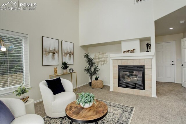 living area featuring a tile fireplace, carpet floors, a high ceiling, and baseboards