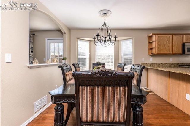 dining space with dark wood-style floors, arched walkways, baseboards, an inviting chandelier, and visible vents