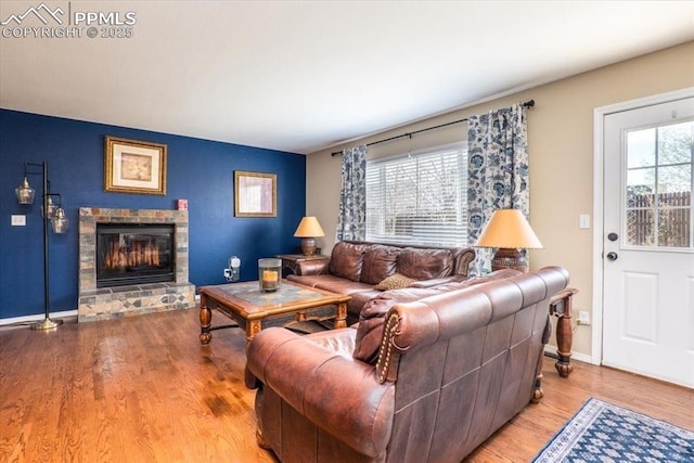living area featuring baseboards, a stone fireplace, and wood finished floors
