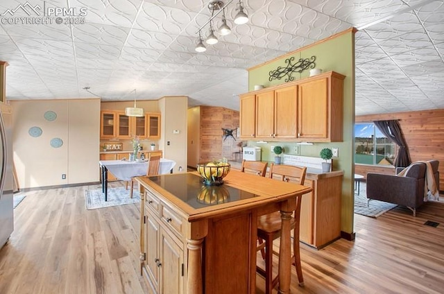 kitchen with light wood-type flooring, wood walls, a kitchen island, and an ornate ceiling