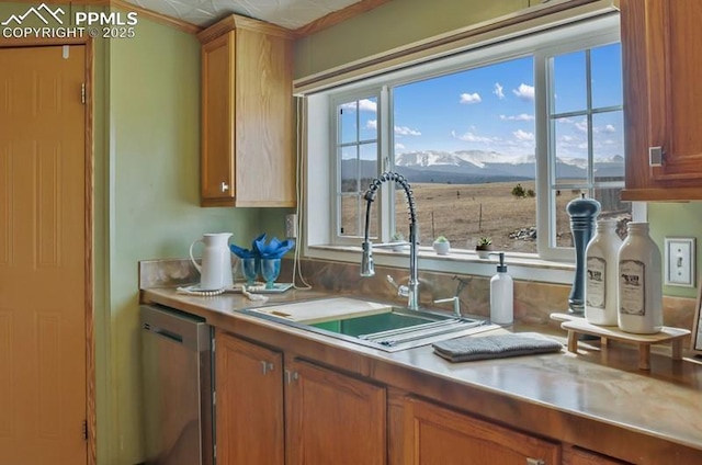 kitchen featuring brown cabinets, light countertops, dishwasher, a sink, and a mountain view