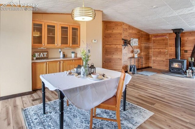 dining room featuring lofted ceiling, wooden walls, a wood stove, baseboards, and light wood-style flooring