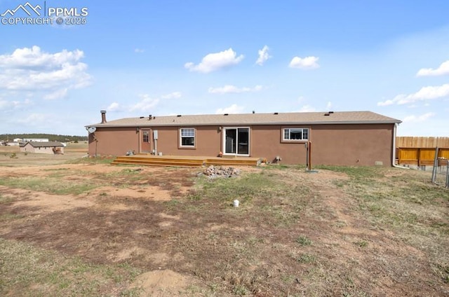 back of house with stucco siding, fence, and a deck