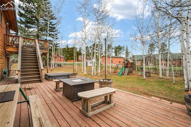 wooden deck featuring a fenced backyard, a fire pit, a playground, stairs, and hot tub deck surround